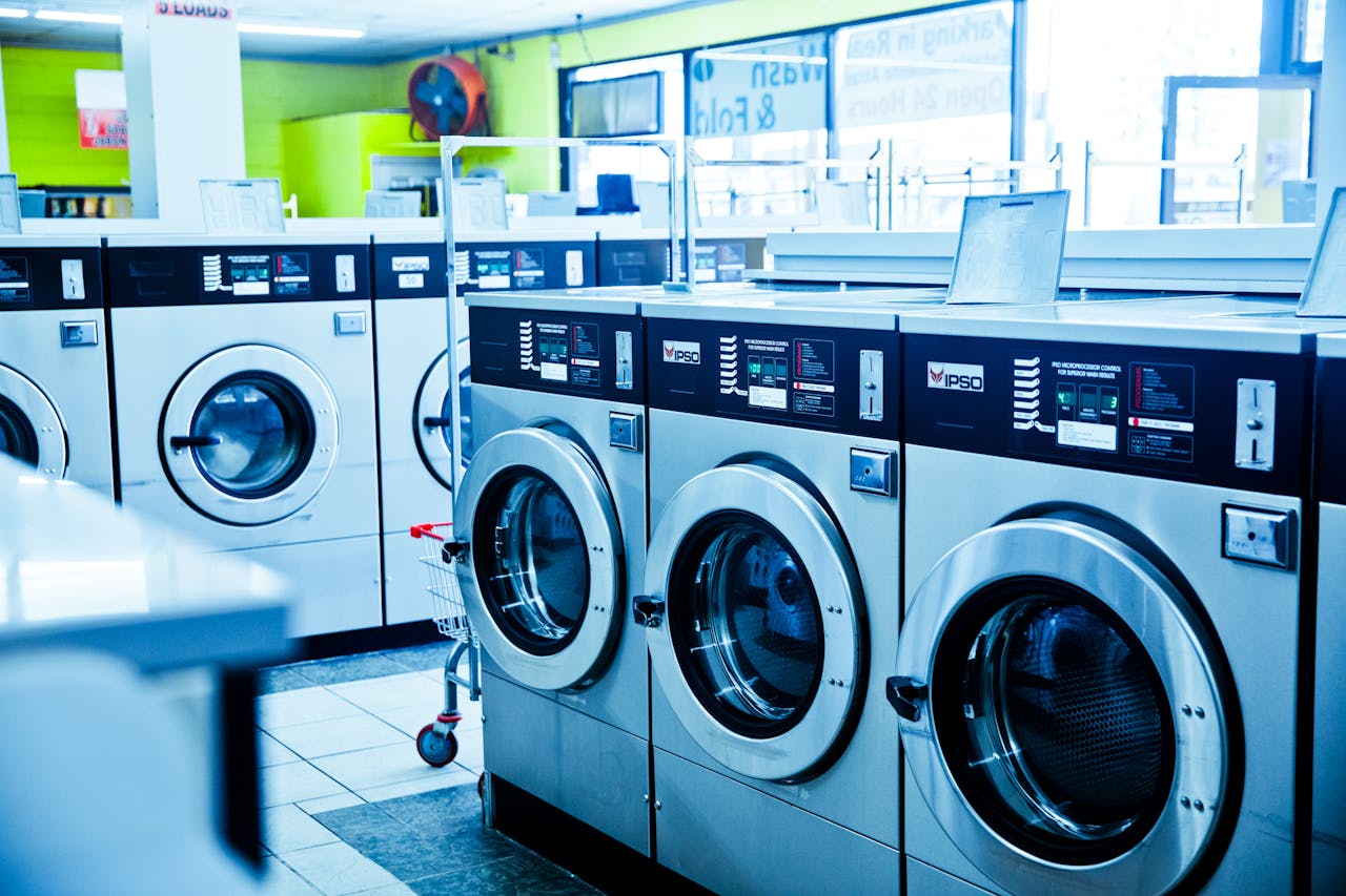 hero-img-01 Contemporary laundromat showcasing a row of industrial washing machines for public use.