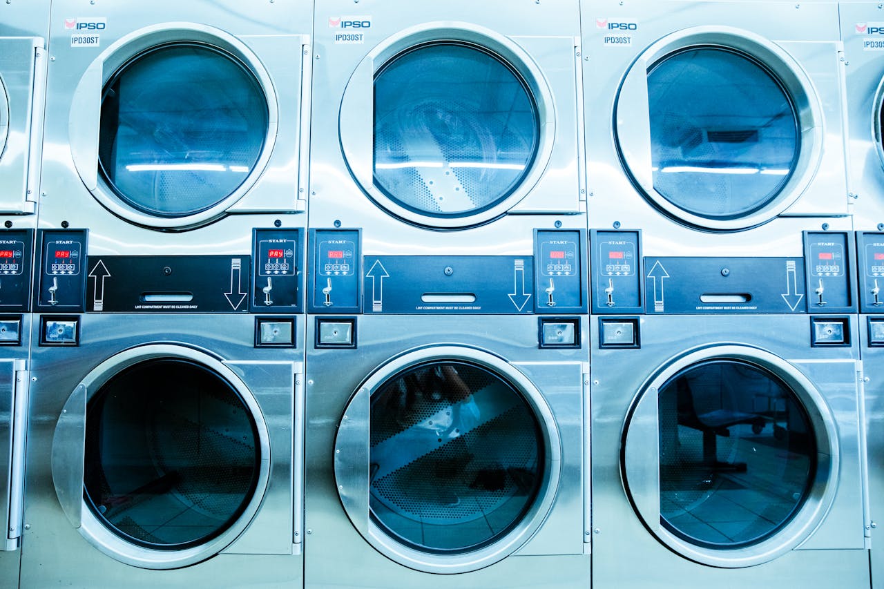 hero-img-02 A row of modern washing machines in a launderette, showcasing contemporary laundry technology.