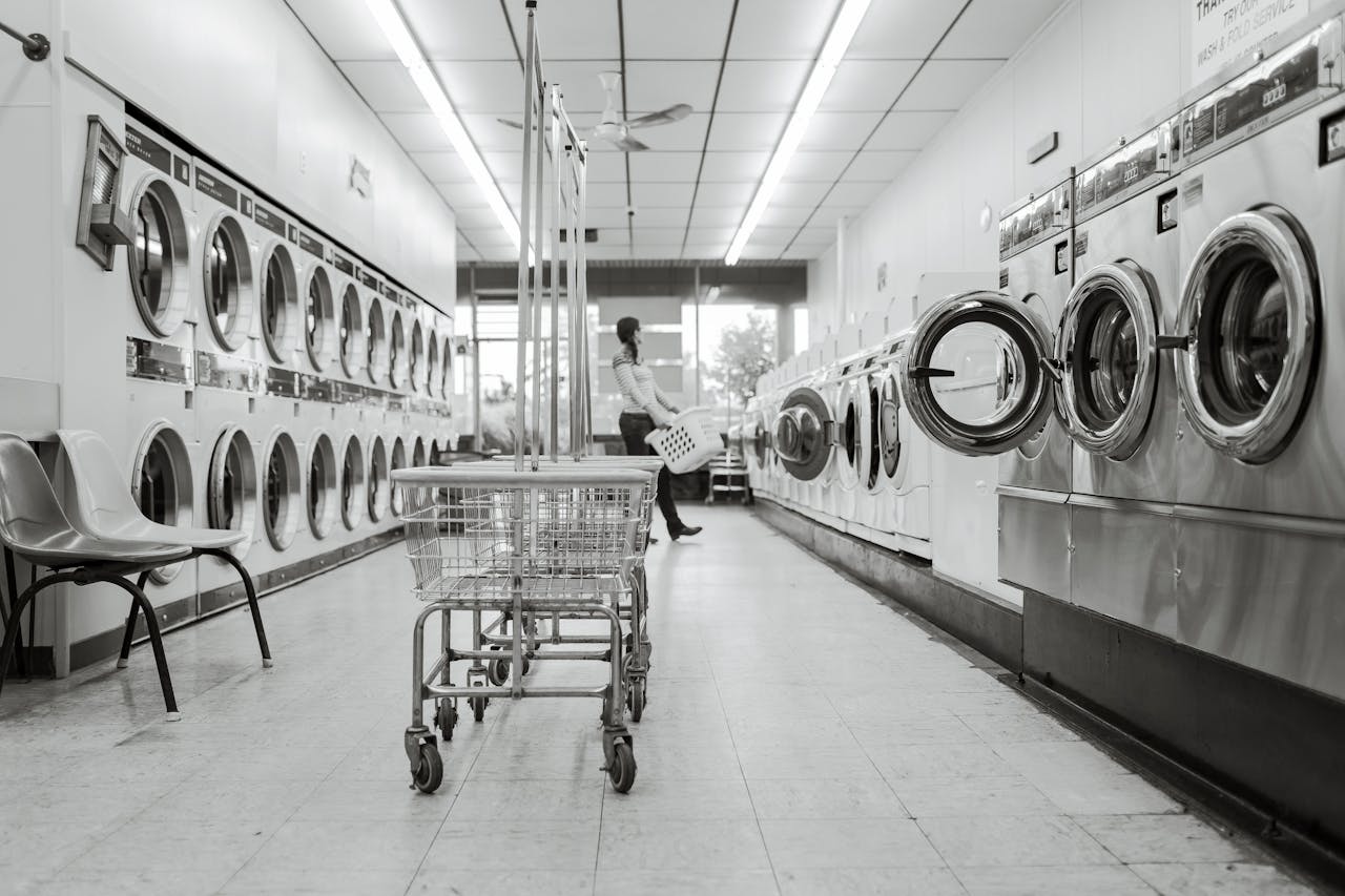 about-01 Black and white image of a laundromat with laundry machines and a person in the background.